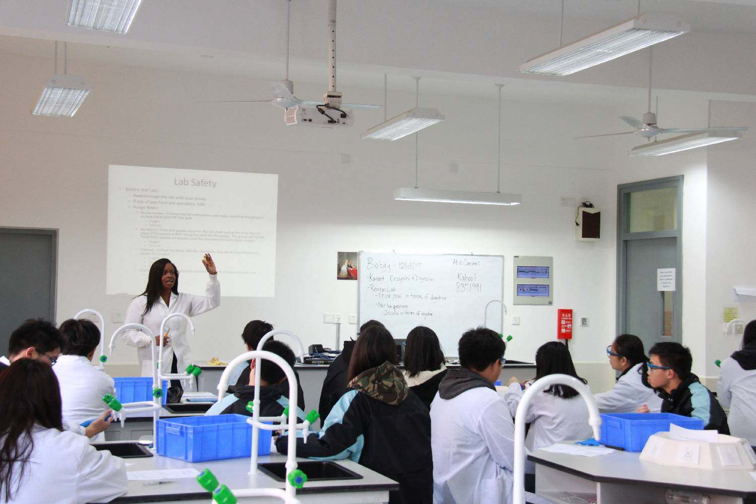 A teacher stands in front of a class of Chinese students, giving a lesson in a science laboratory