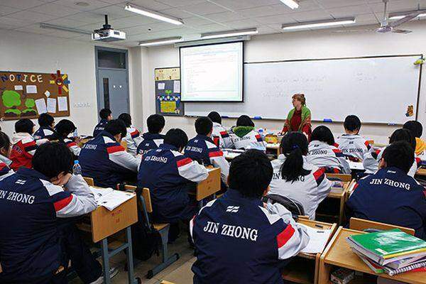 A mathematics teacher in front of whiteboard speaks to a class of Chinese students sitting in rows of desks