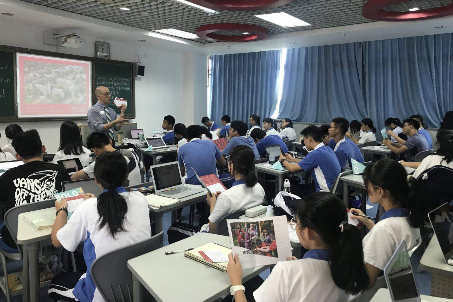 A teacher gives a presentation to a classroom full of Chinese students sitting at desks