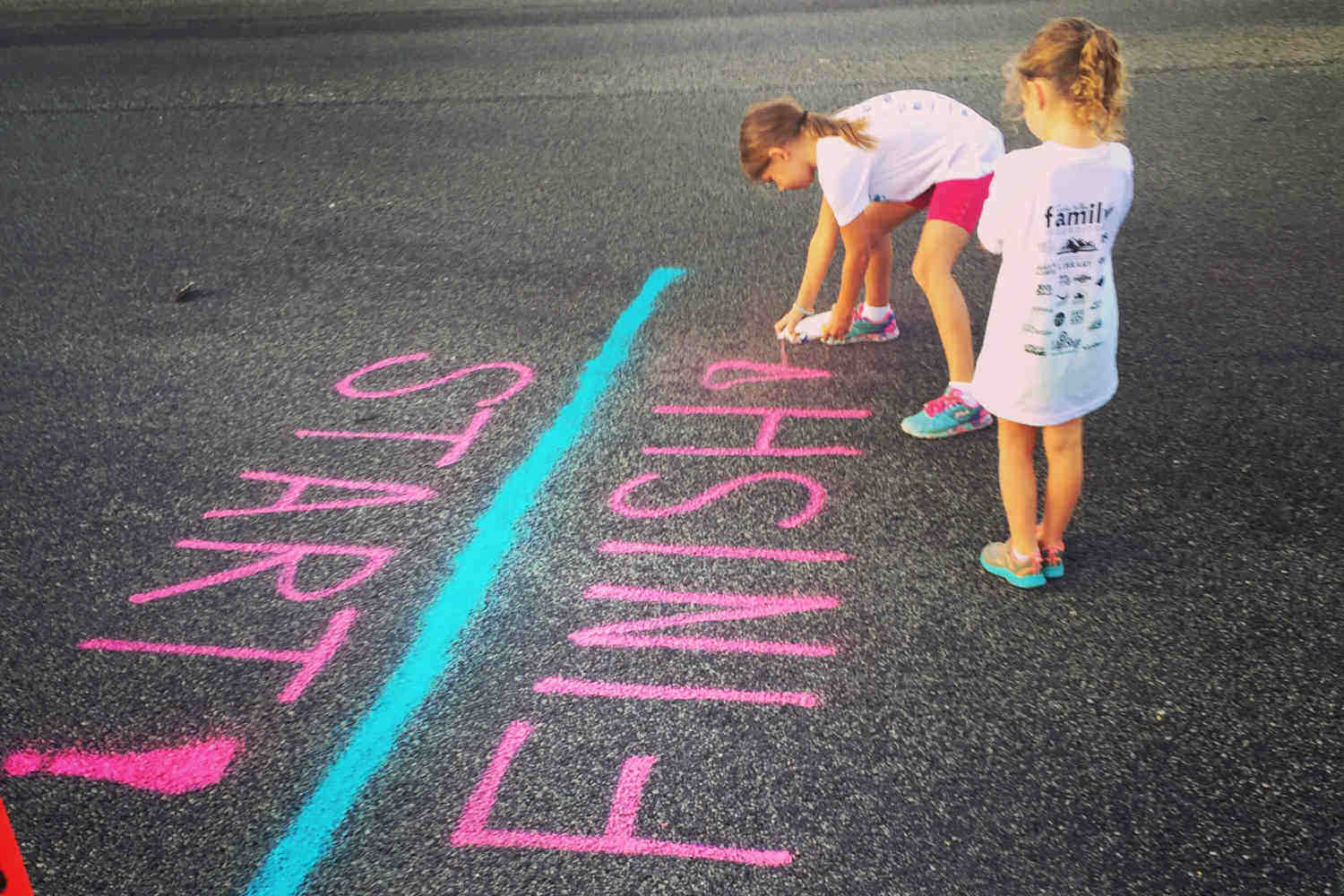 Children stand next to the words start and finish written on the ground in chalk